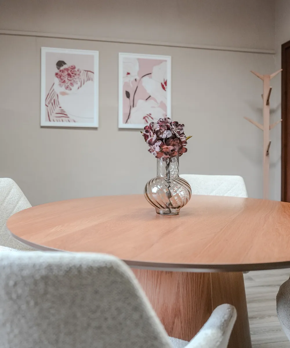 Besprechungsraum mit rundem Holztisch, Blumenvase und zwei Bildern an der Wand